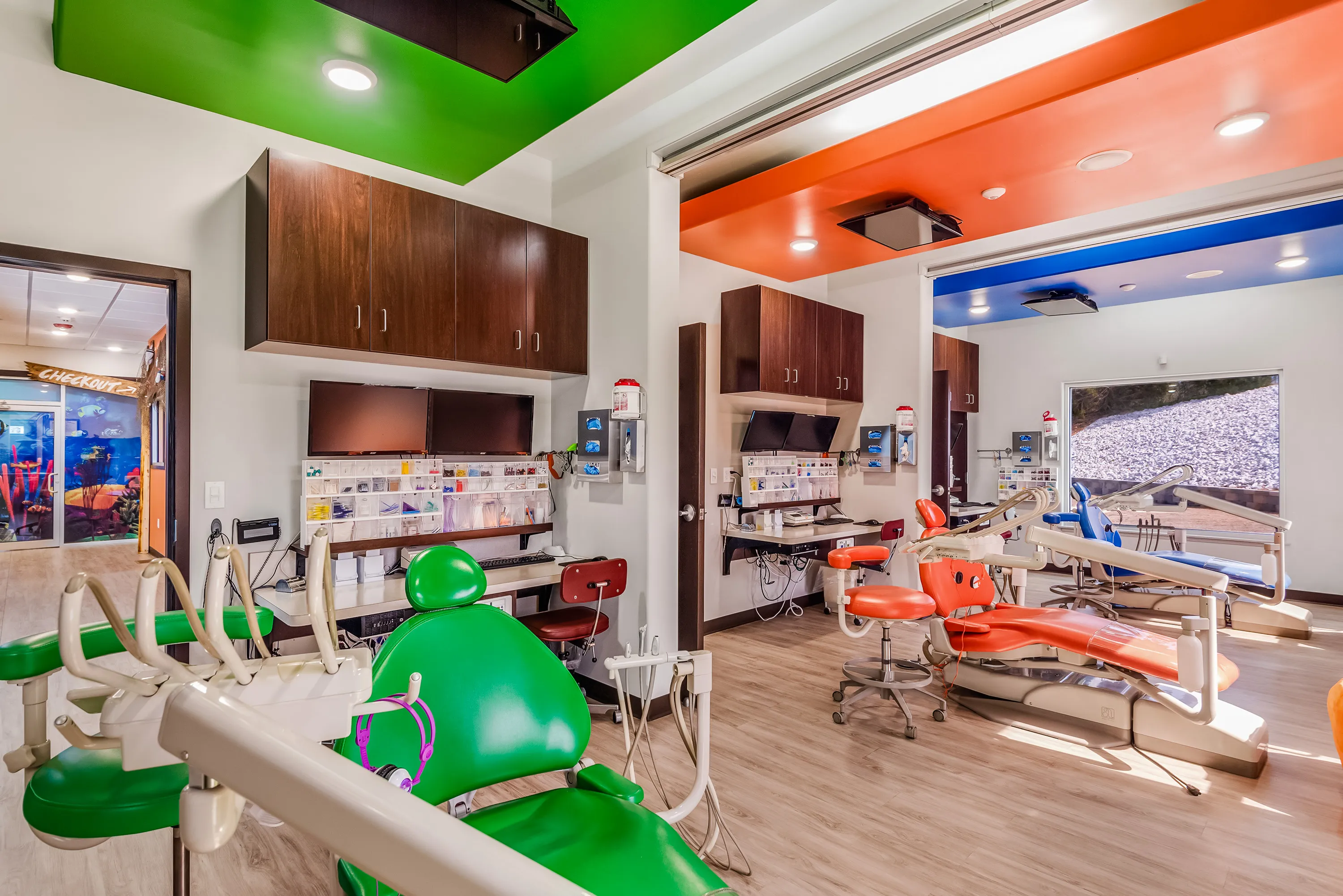 A Super Smiles operatory with green and orange painted ceiling bays above the treatment chairs