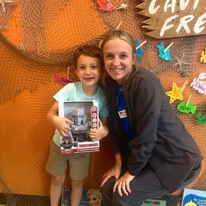 A young Cavity Free Club winner holding a Transformers prize, with a Super Smiles team member, in front of the Cavity Free Club wall