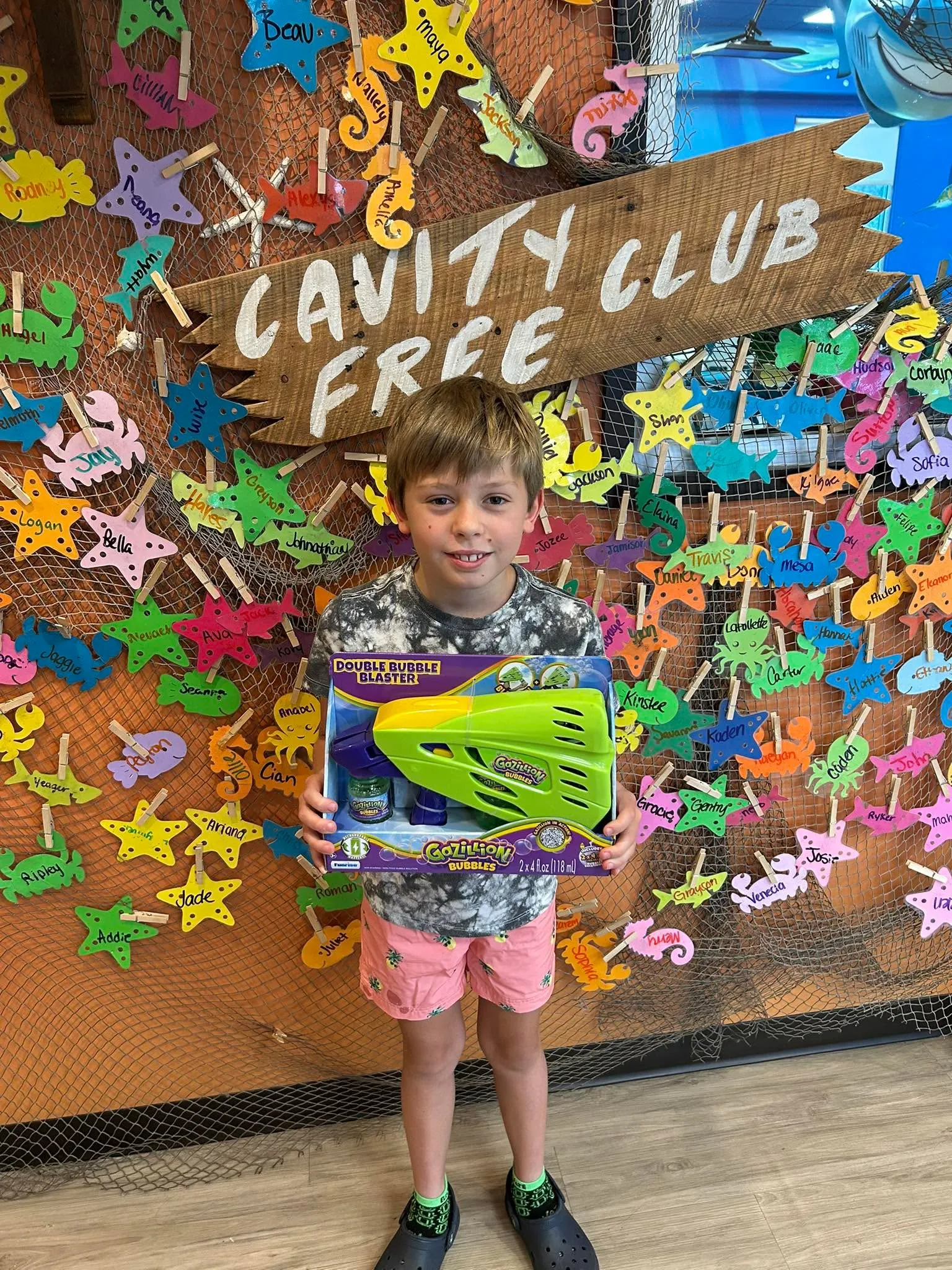 A young patient with a foam-blaster prize in front of the Cavity Free Club sign